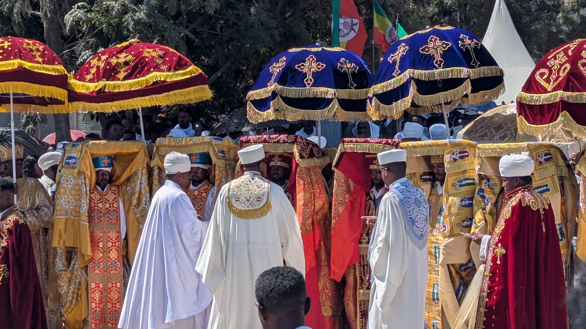 Priests in embroidered robes carry the tabots under liturgical umbrellas at Timket